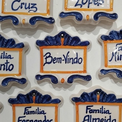 Placas decorativas em cerâmica com nomes de famílias em azul, branco e laranja.