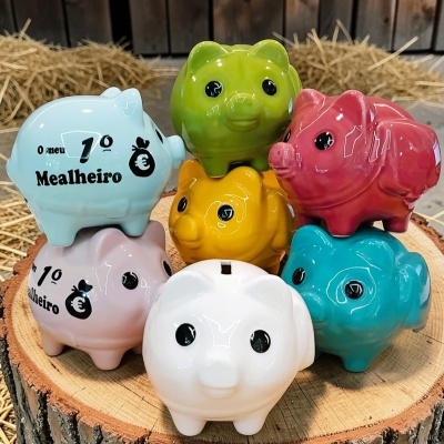 Conjunto de mealheiros cerâmicos coloridos em forma de porquinho empilhados sobre um tronco de árvore