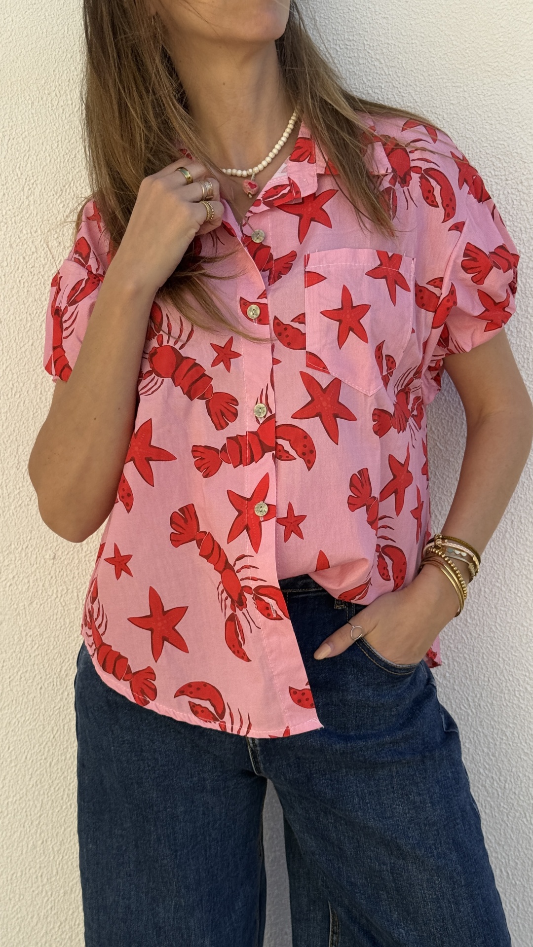 Blusa rosa com padrão vermelho de lagostas e estrelas do mar, botões brancos, combiada com calças de ganga escuras