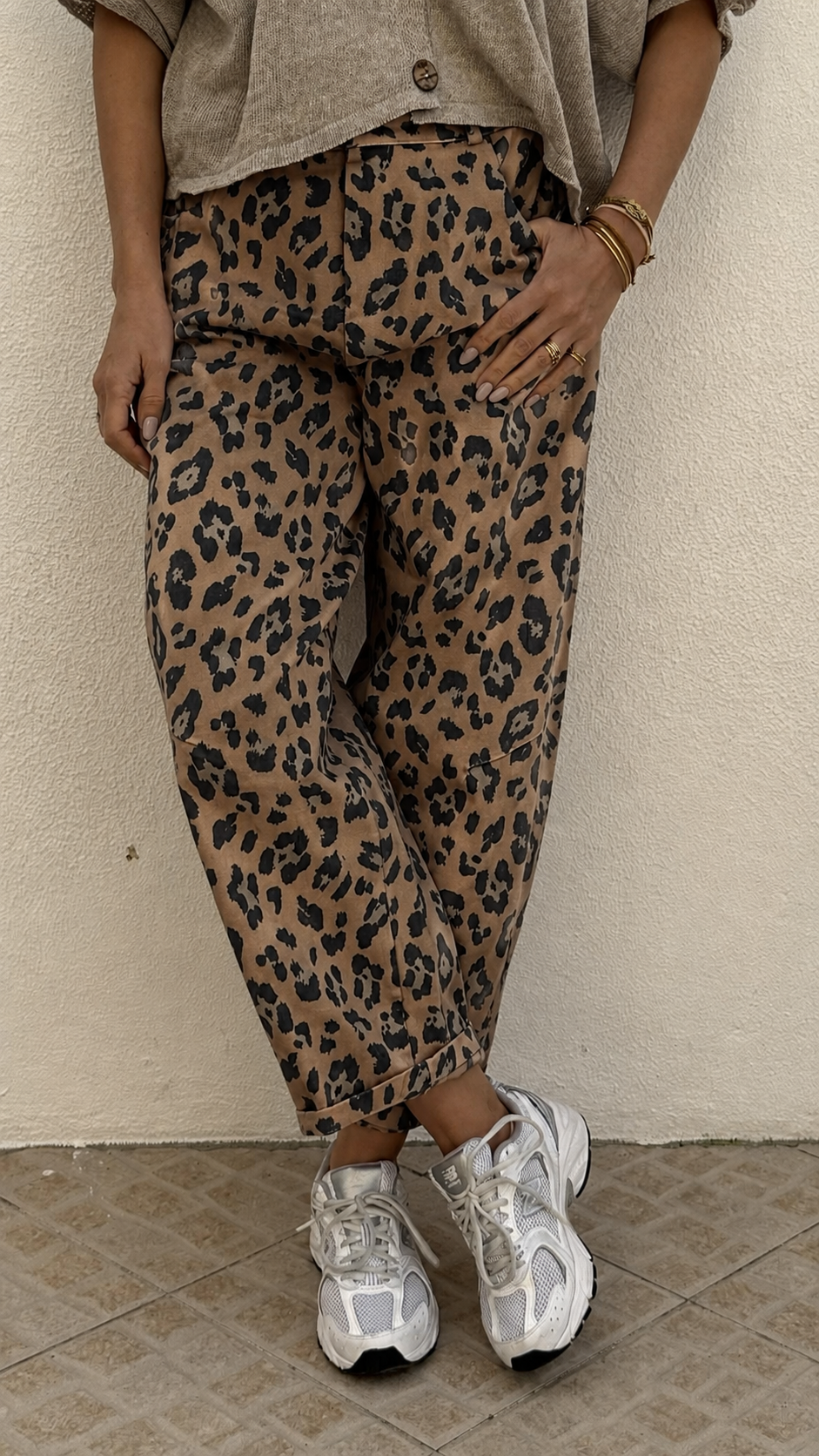 Calças com padrão animal print castanho e preto e ténis desportivos brancos.