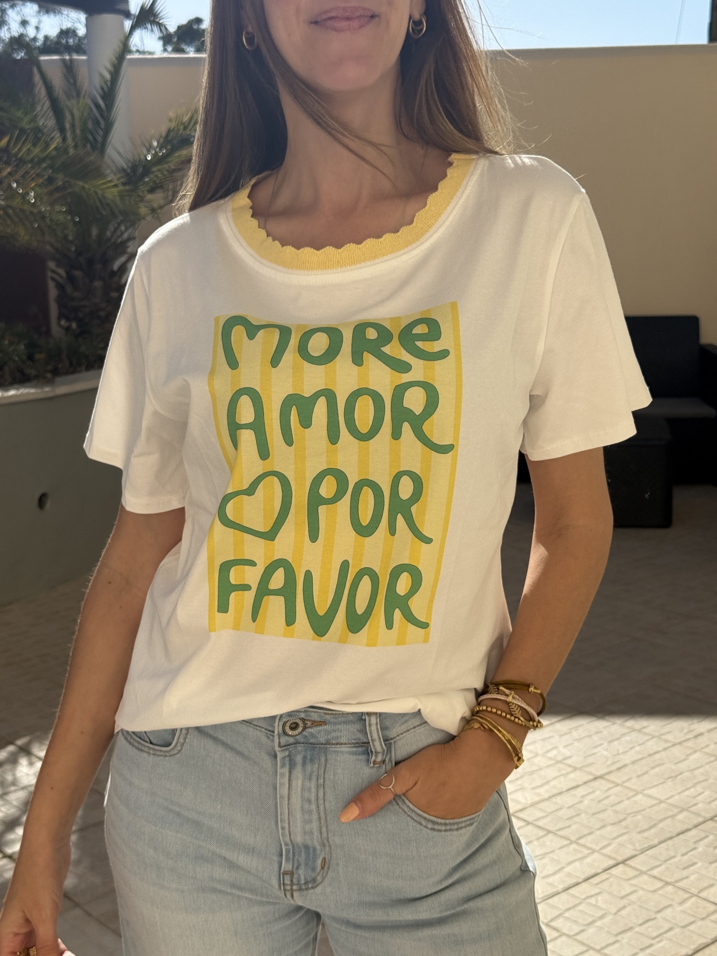 T-shirt branca com estampa colorida e texto, usada com jeans claros em ambiente exterior.