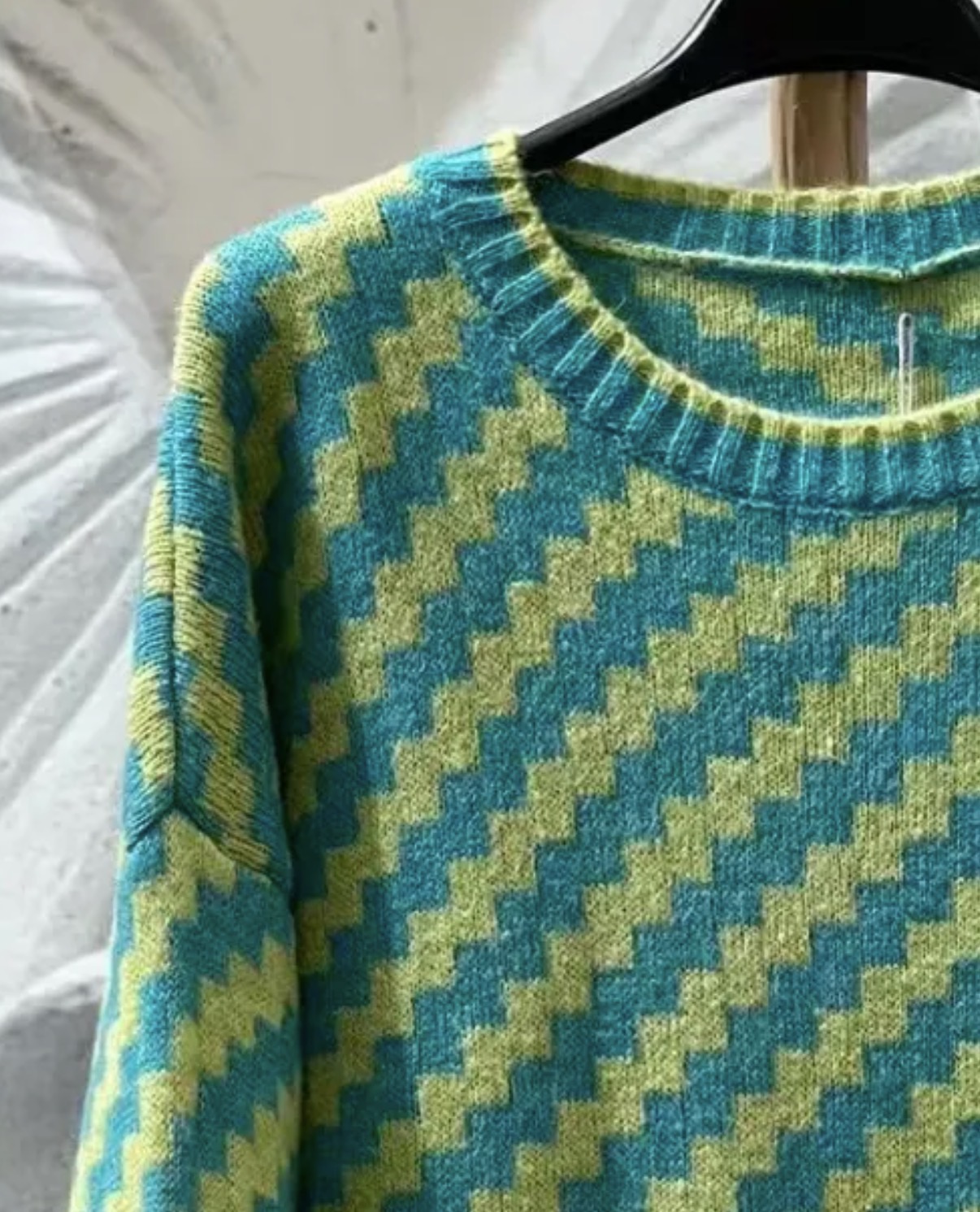 Camisola de malha azul e verde com padrão geométrico pendurada