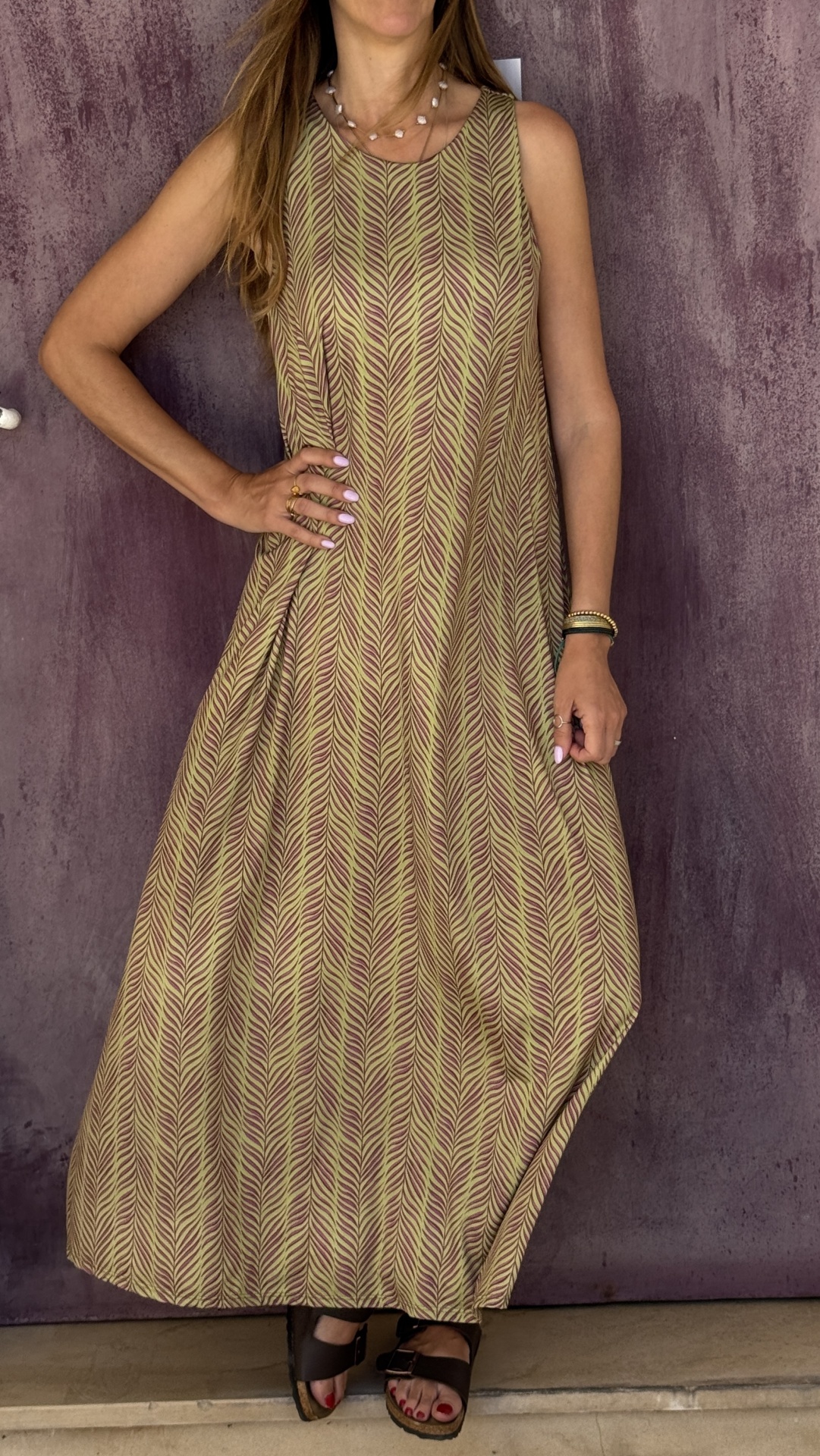 Vestido longo com padrão de folhas verde-lima e roxo, leve, usado por mulher com sandálias castanhas