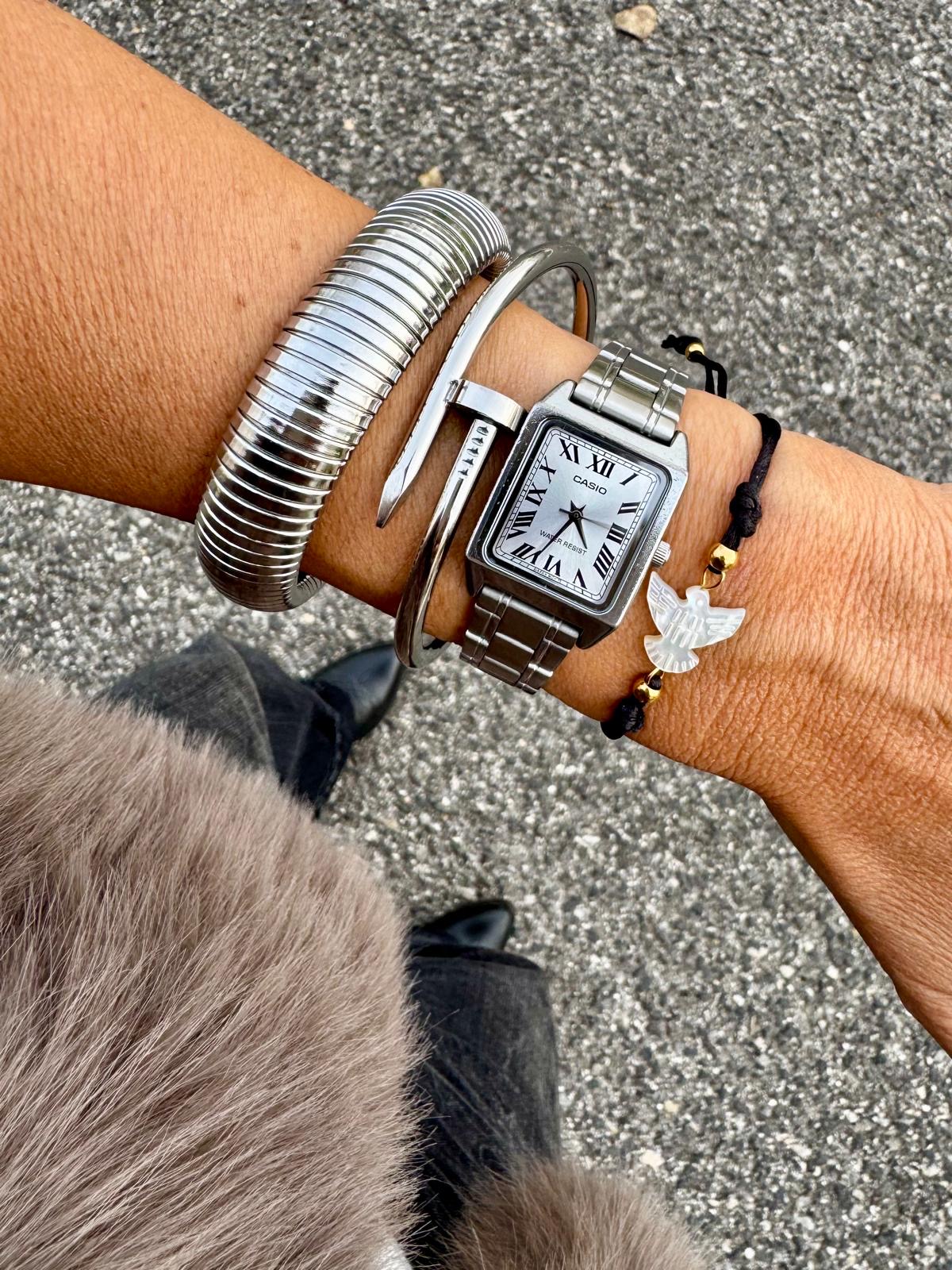 Pulso com relógio prateado e três pulseiras em pavimento cinzento