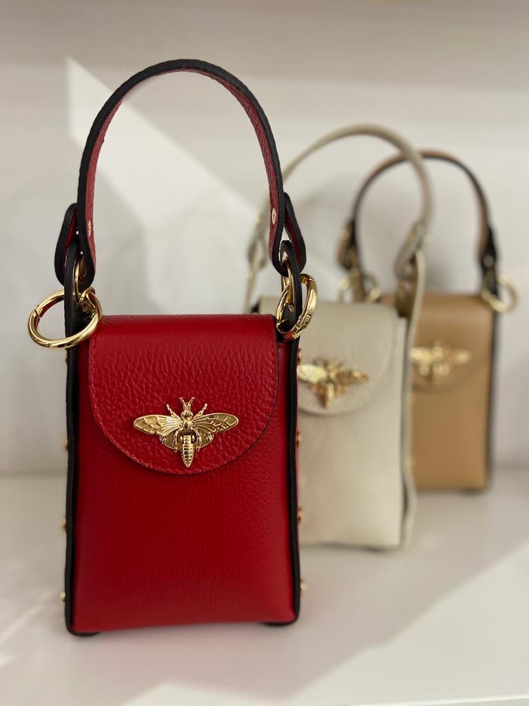 Três malas de mão pequenas em pele vermelha, branca e bege com aplicação dourada de abelha.