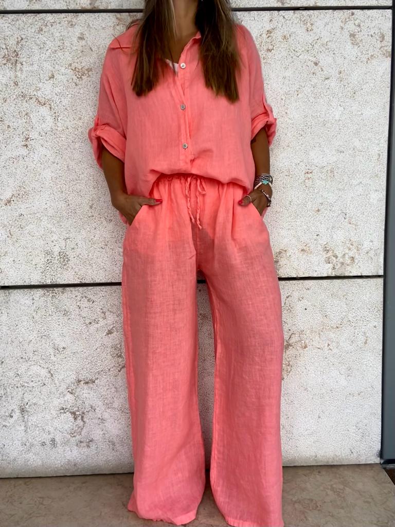 Conjunto feminino coral de linho composto por camisa e calças largas contra parede clara