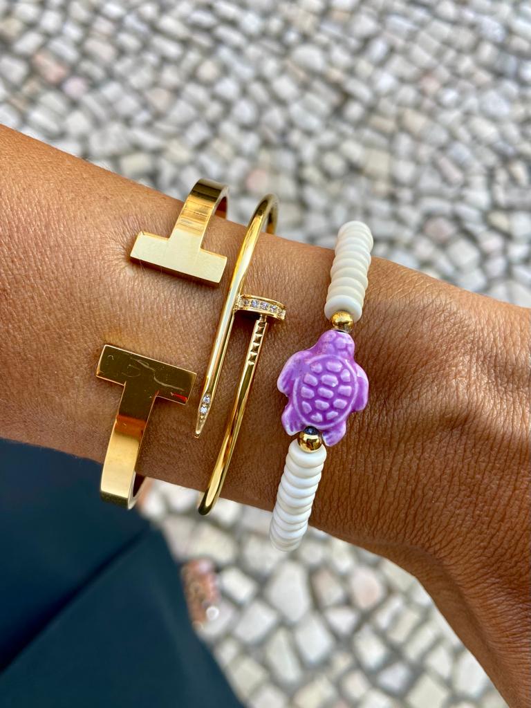 Pulseiras douradas e pulseira com contas brancas e tartaruga roxa no pulso.