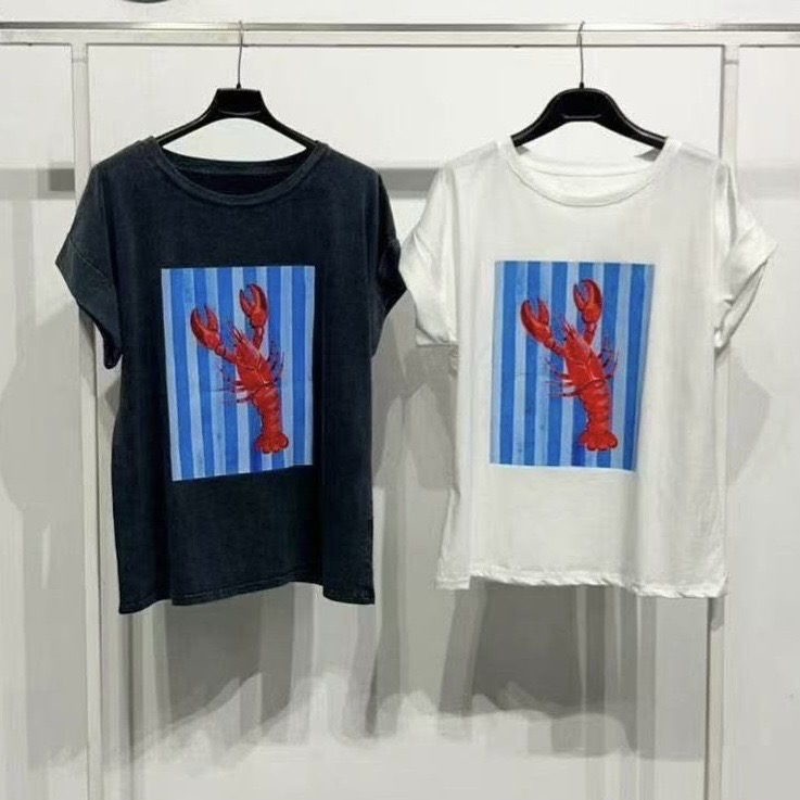 Duas t-shirts, preta e branca, com estampa de lagosta vermelha em fundo riscado azul e branco