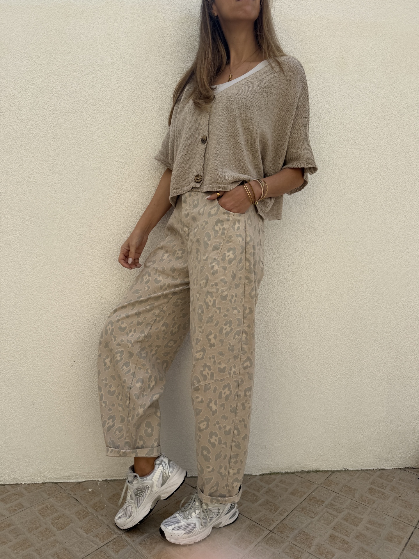 Mulher vestindo casaco bege de malha, camisa branca, calças largas bege com padrão de onça e sapatos desportivos brancos prateados
