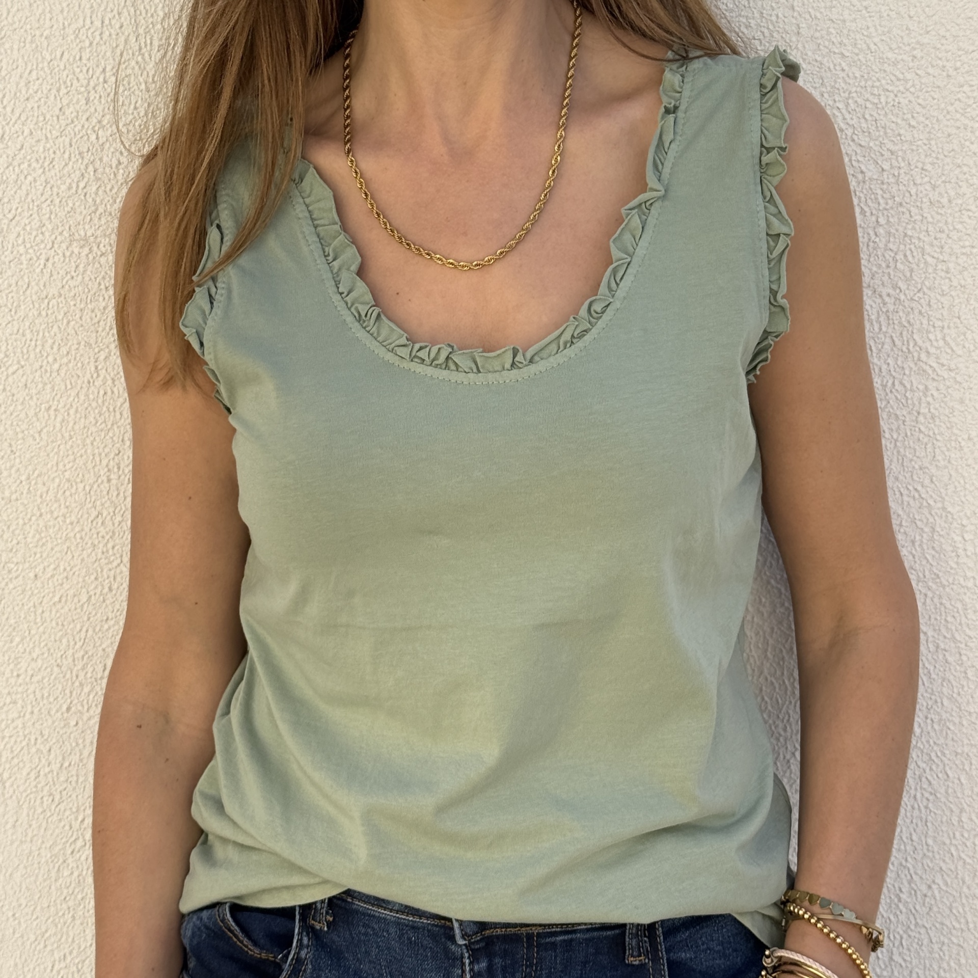 Top verde claro com folhos nas alças e decote, acessórios dourados no pescoço e pulsos.