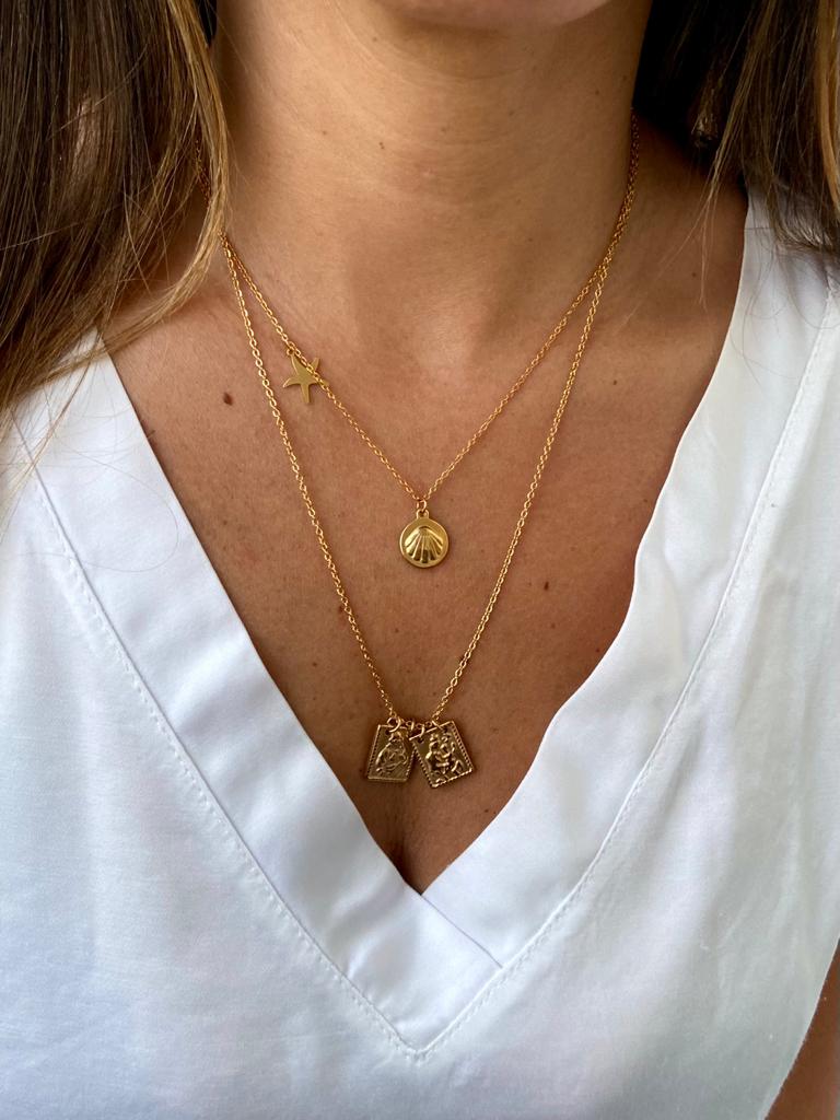 Colares dourados femininos em cascata com pingentes variados sobre blusa branca.