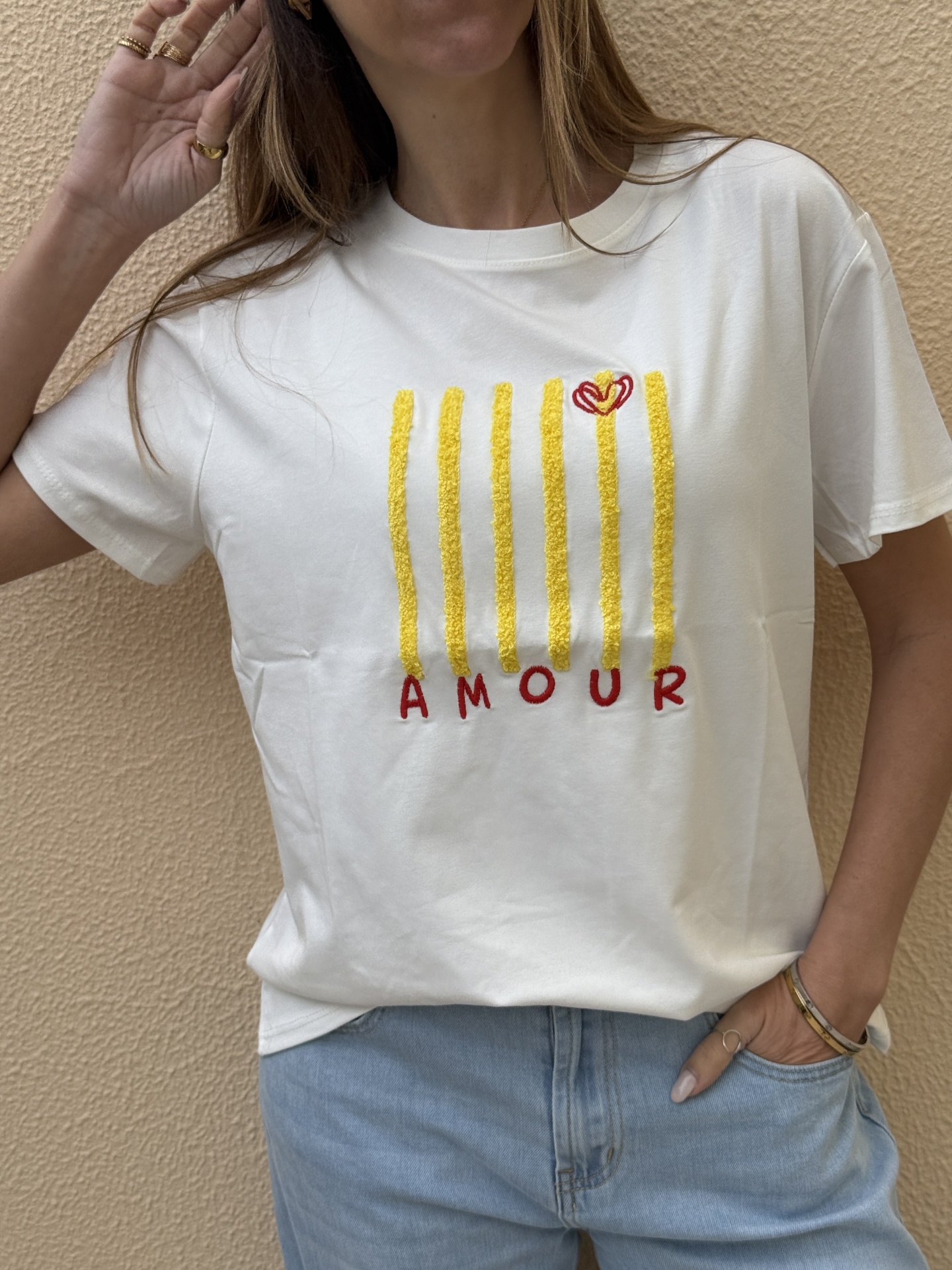T-shirt branca decorada com riscas amarelas e palavra AMOUR em vermelho