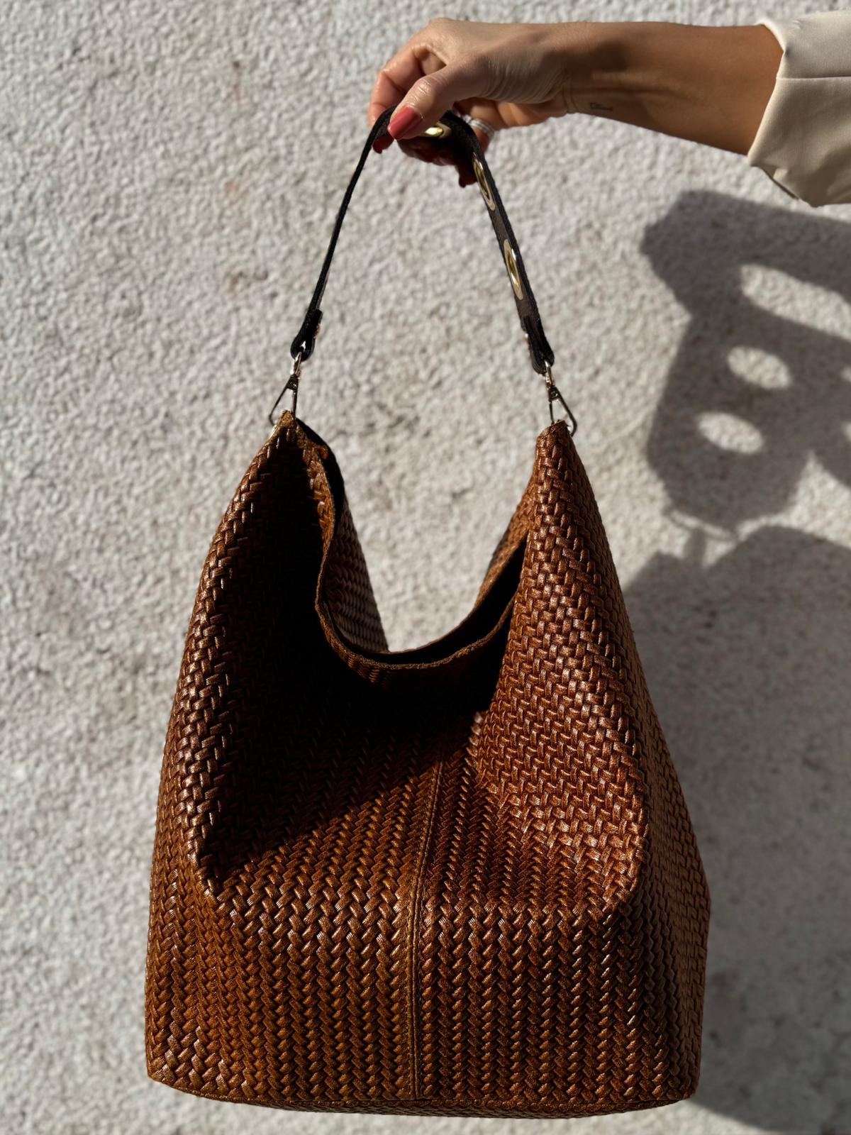 Mala de mão castanha trançada com alça preta suspensa em fundo claro