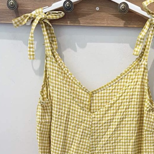 Vestido amarelo xadrez em cabide branco num suporte de madeira