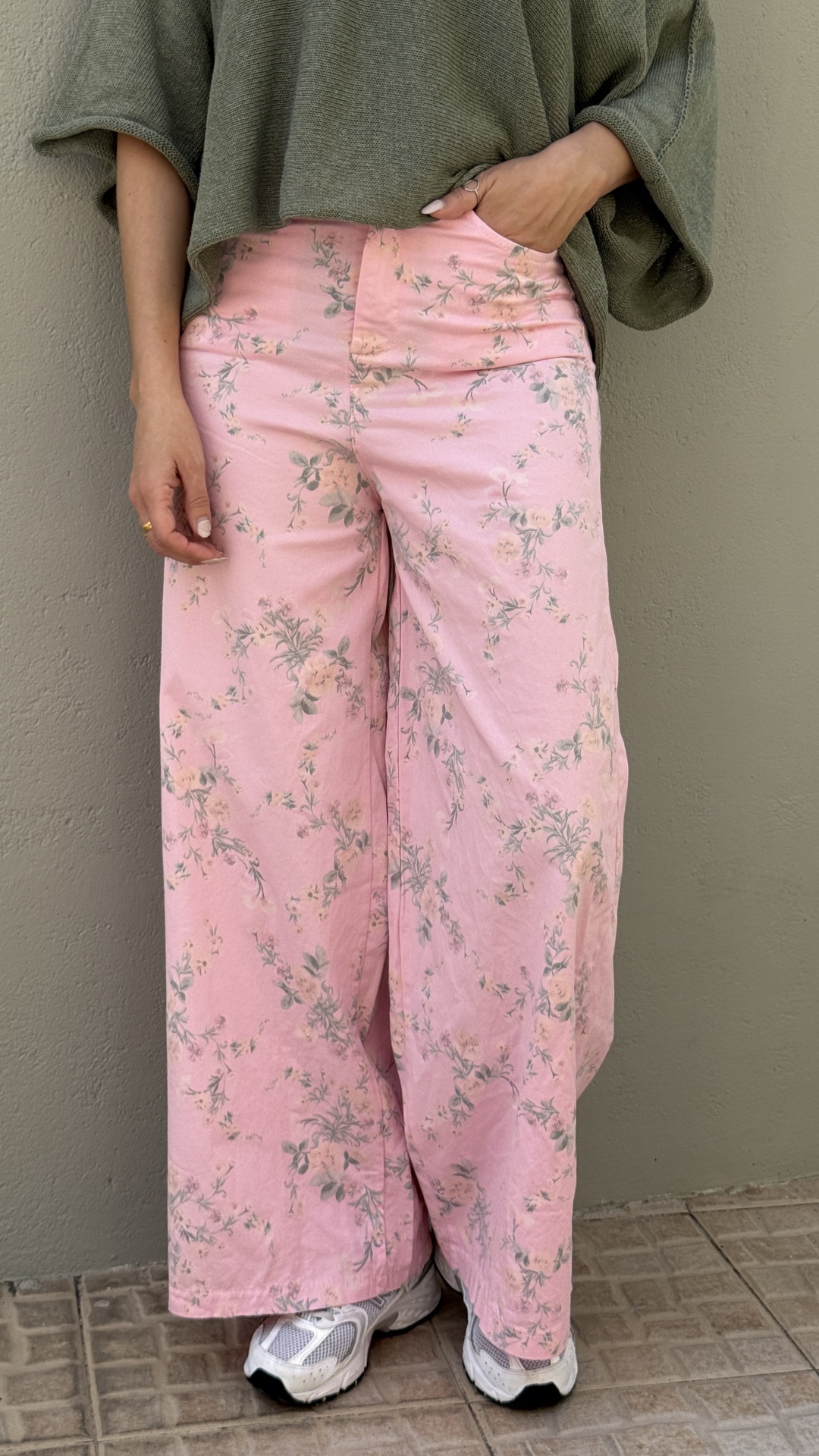 Calças rosa com padrão floral usadas por pessoa com camisa verde e sapatilhas brancas
