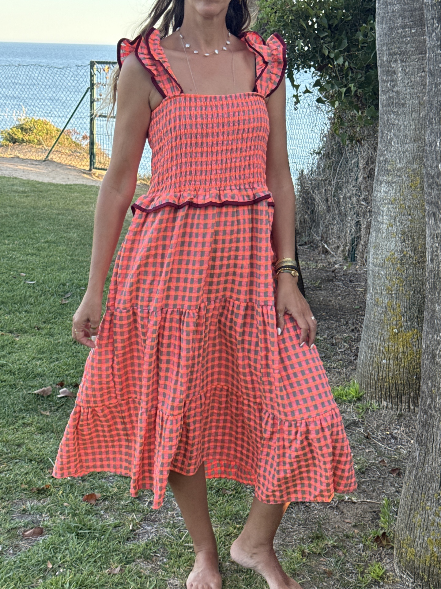 Vestido midi xadrez vermelho e rosa com folhos e remates vinho, usado por mulher ao ar livre