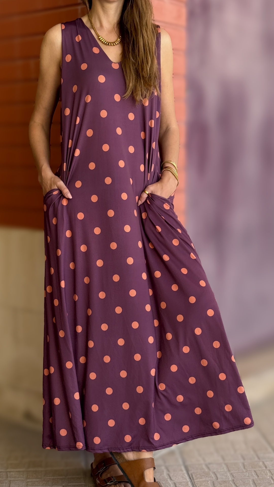 Vestido roxo com bolinhas laranjas e bolsos, sandálias castanhas, acessórios dourados.