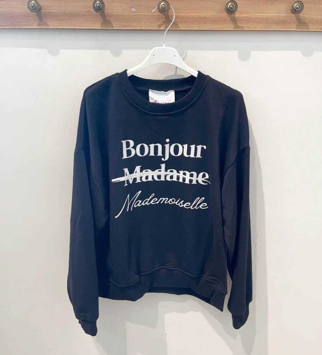 Sweatshirt preta com texto branco 'Bonjour Madame' riscado e 'Mademoiselle' escrito abaixo pendurada
