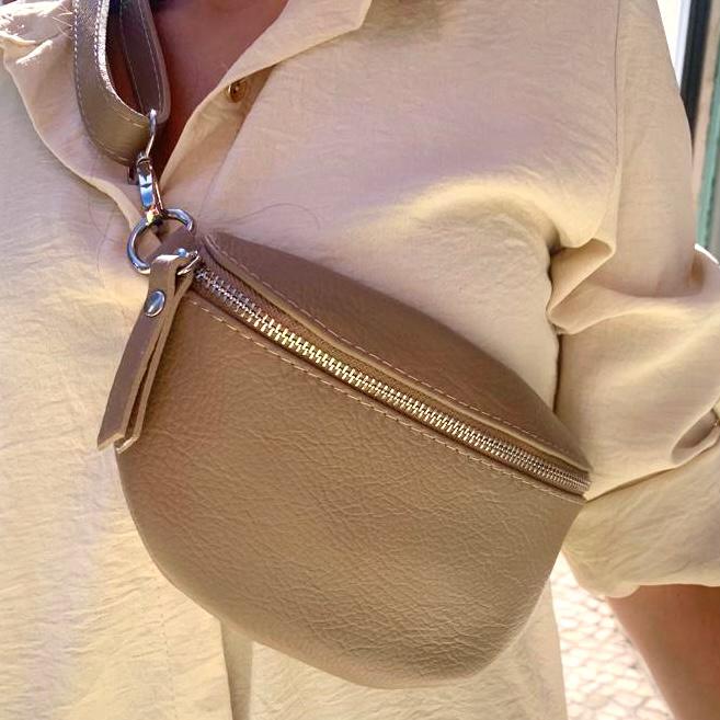 Bolsa bege de cinto em pele sintética com fecho dourado usada sobre camisa creme