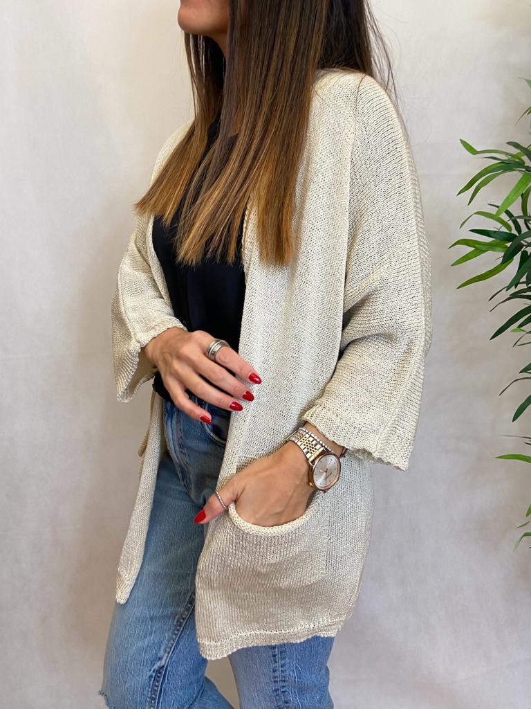 Casaco bege de malha com bolso e manga 3/4 usado por mulher com camiseta preta e calças de ganga