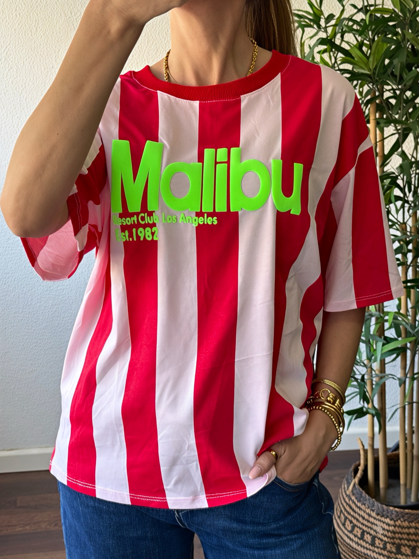 T-shirt de riscas vermelhas e brancas com texto verde neón, vestida por pessoa com pulseiras douradas
