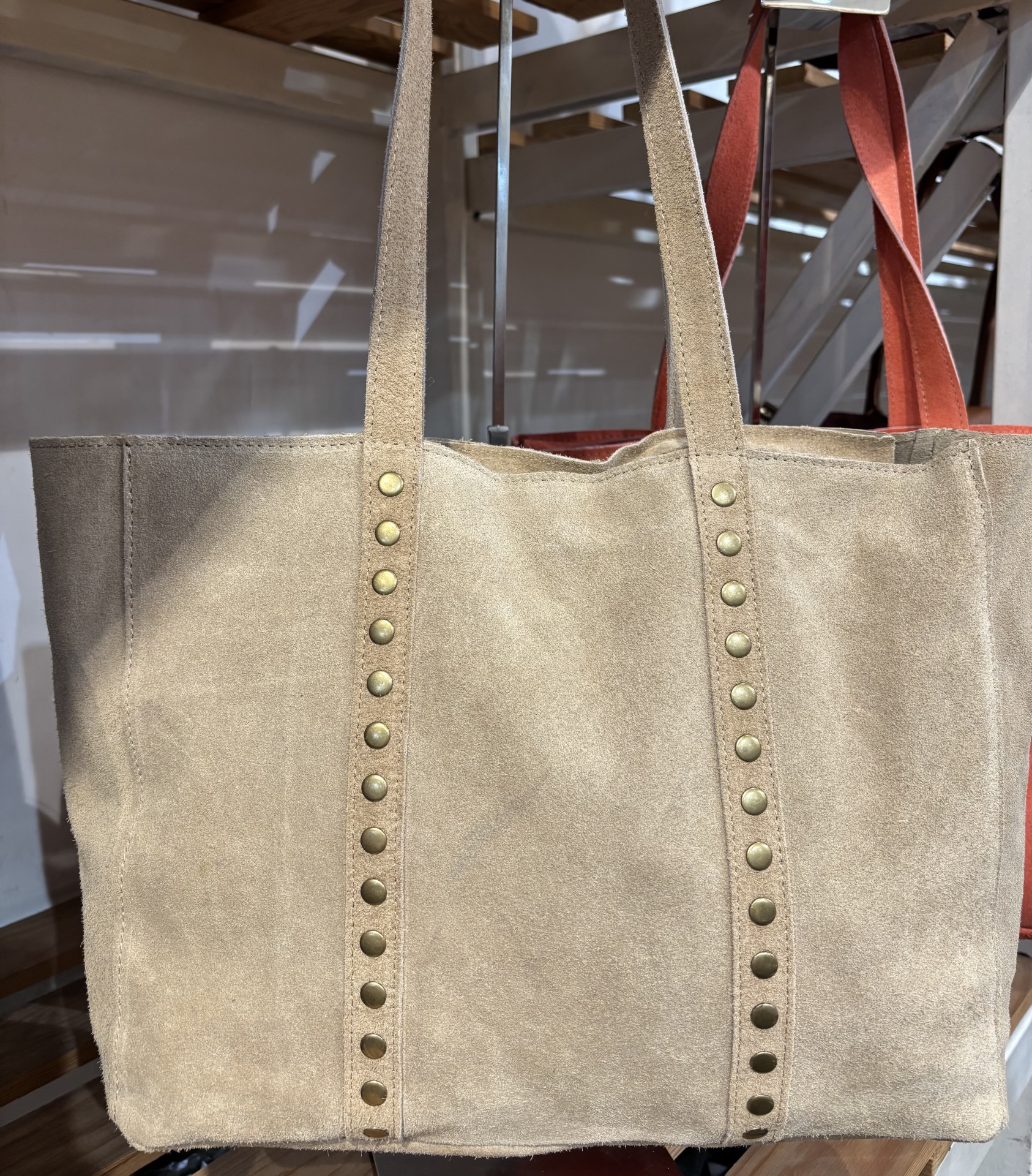 Mala bege de camurça com tachas douradas, exposta em loja