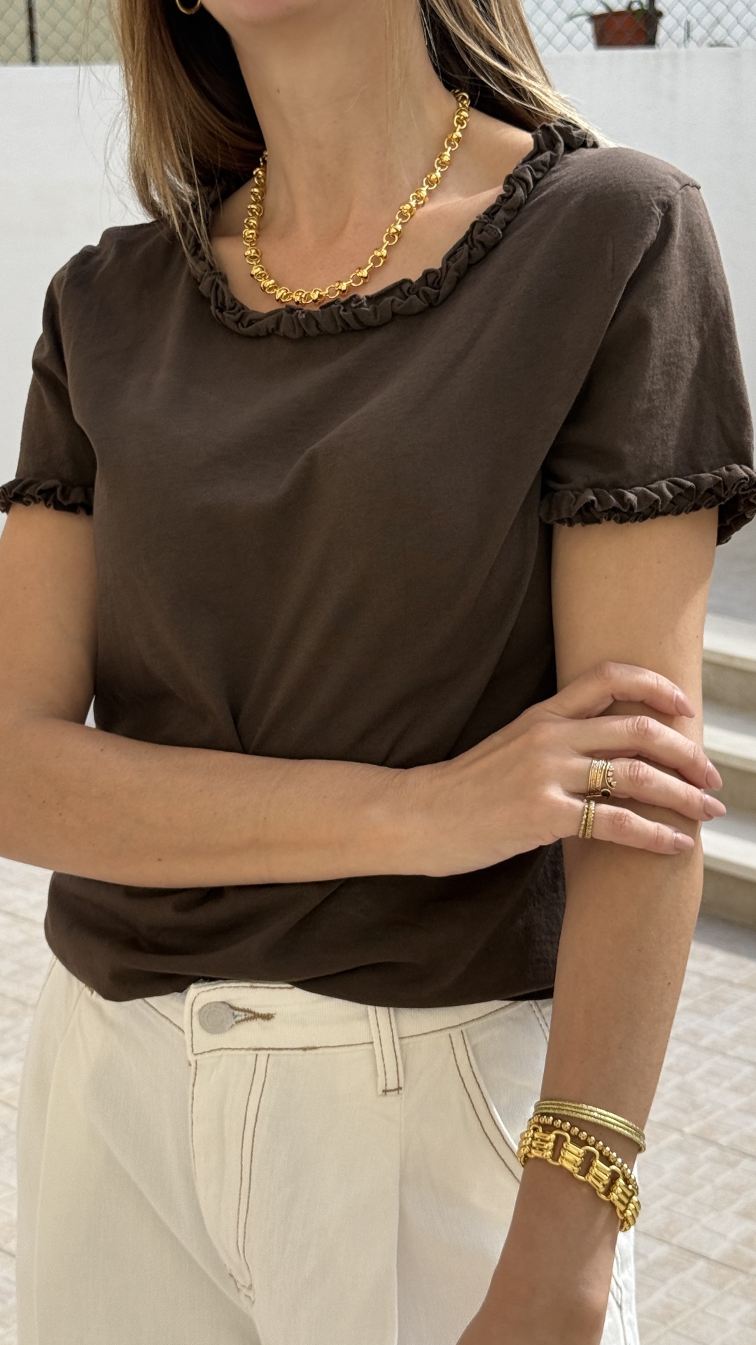 Mulher com t-shirt castanha e acessórios dourados