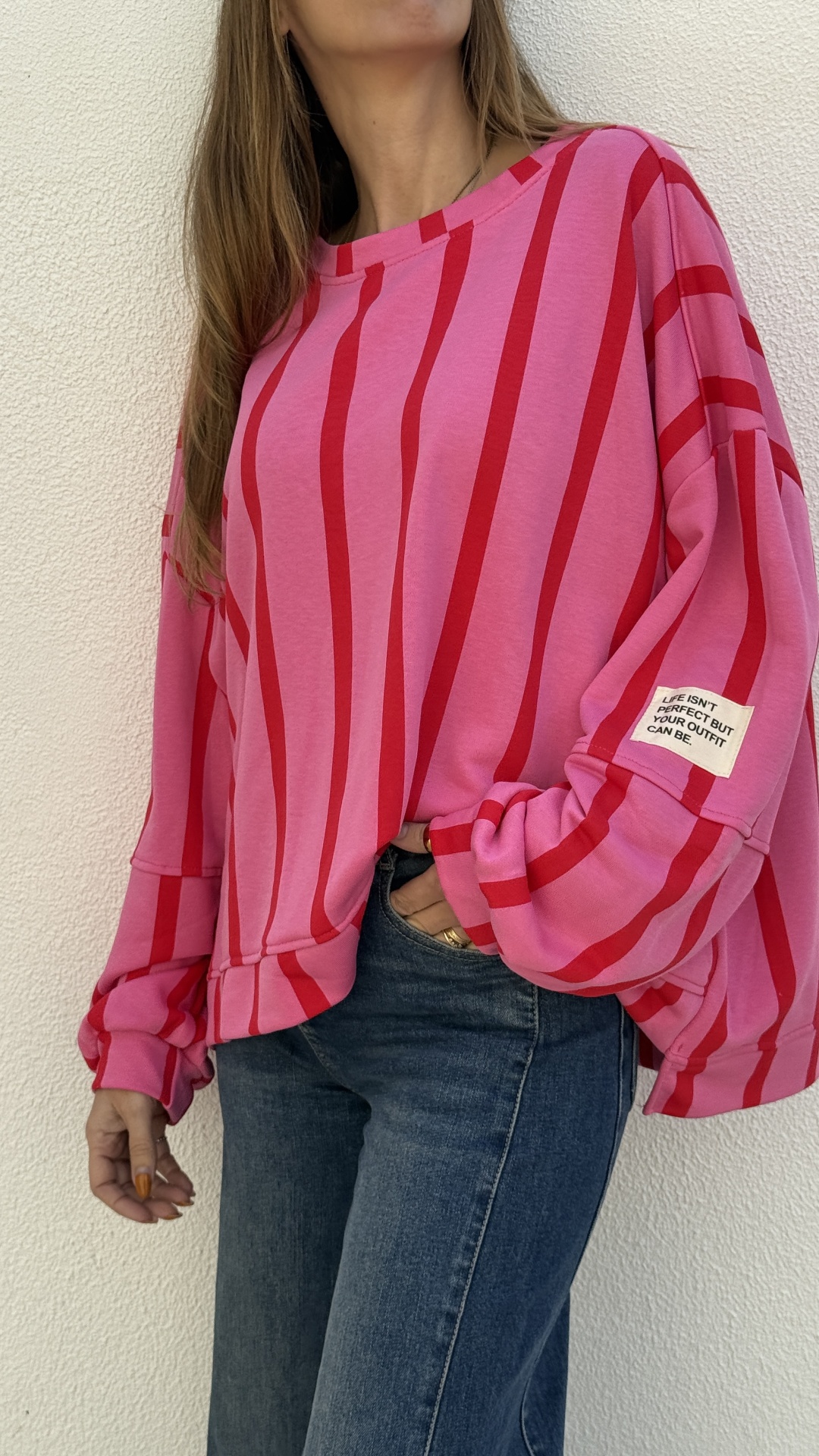Camisola rosa de riscas vermelhas com etiqueta na manga e jeans azuis.