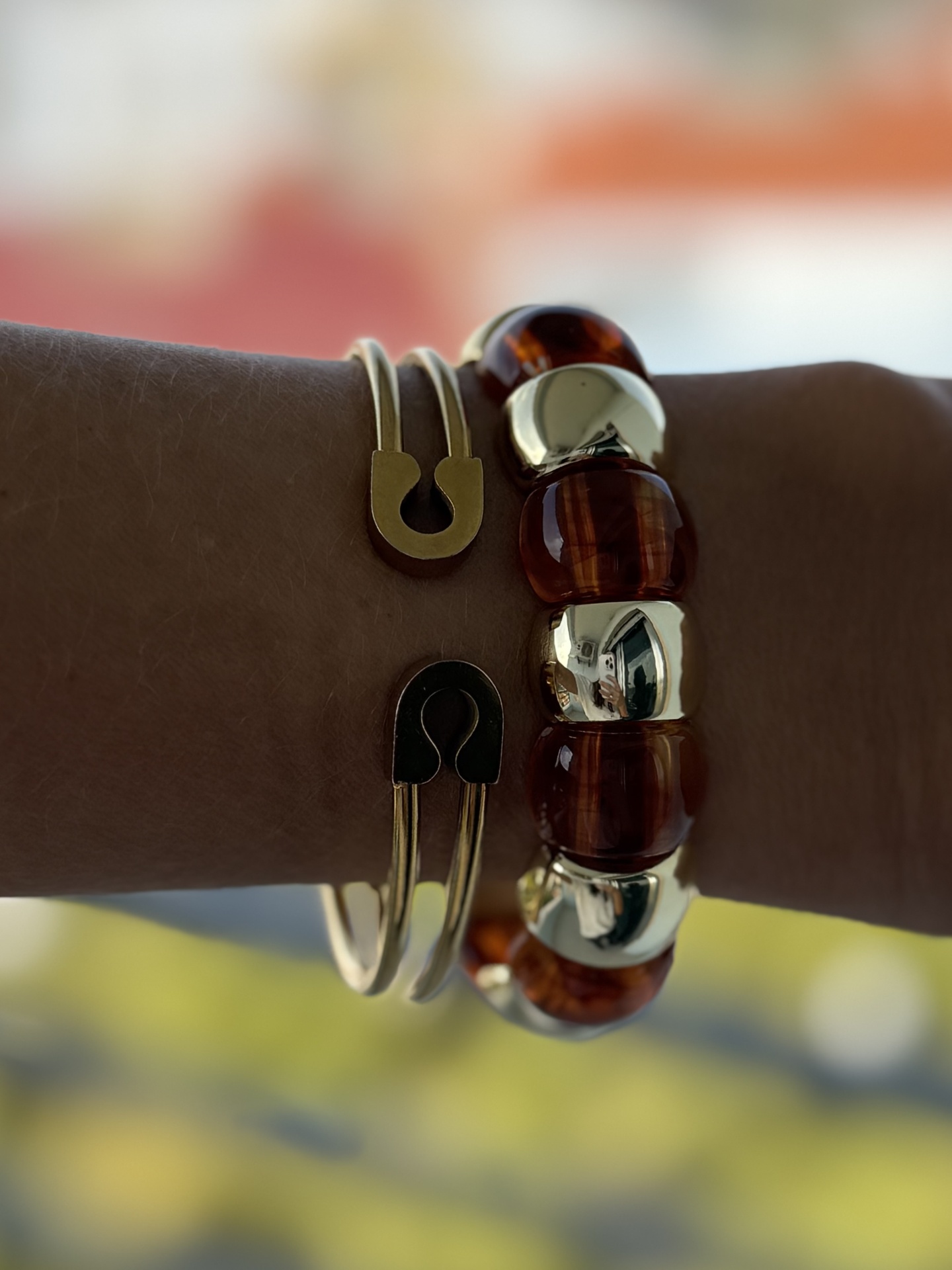 Dois pulseiras no pulso, uma com contas âmbar e douradas e outra dourada com detalhes em ferradura