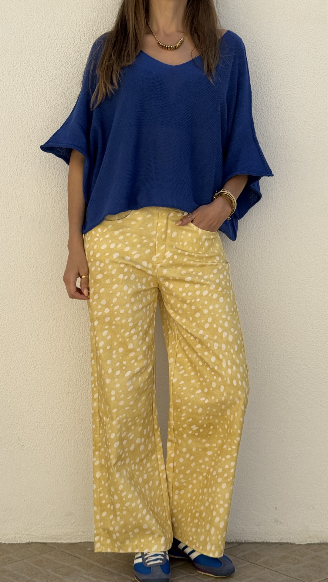 Calças amarelas largas com padrão branco, blusa azul escura de manga larga e ténis azuis.