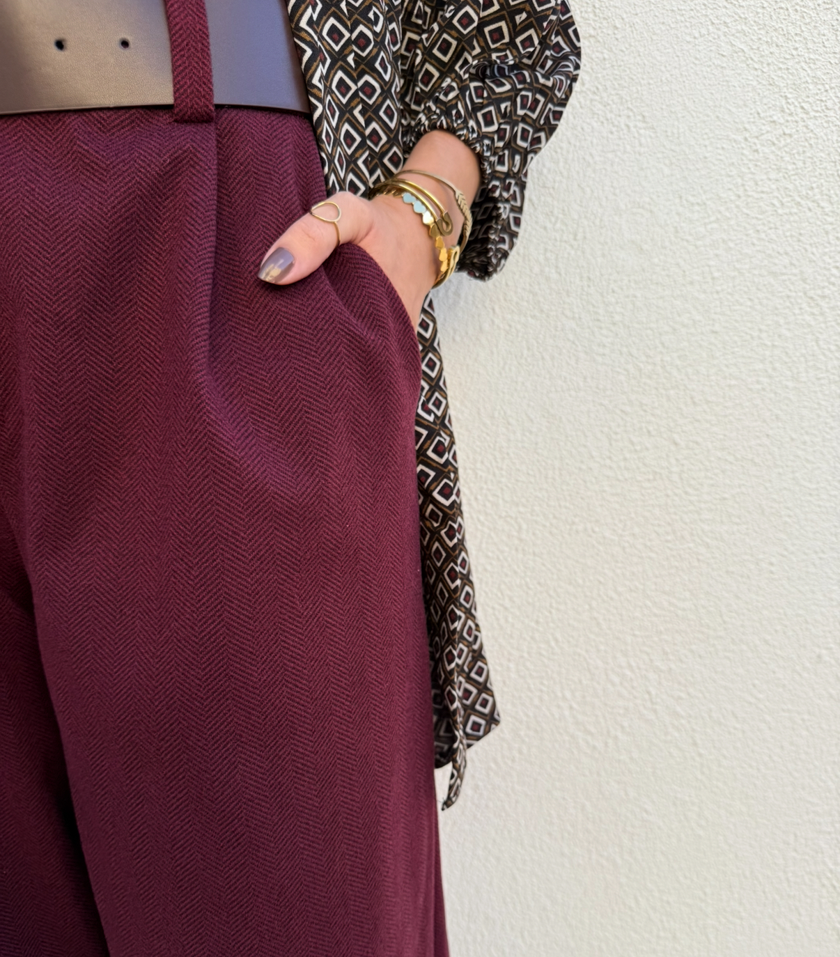 Calças ou saia bordeaux com padrão espinha de peixe, cinto castanho, blusa com padrão geométrico, pulseiras douradas e anel no dedo