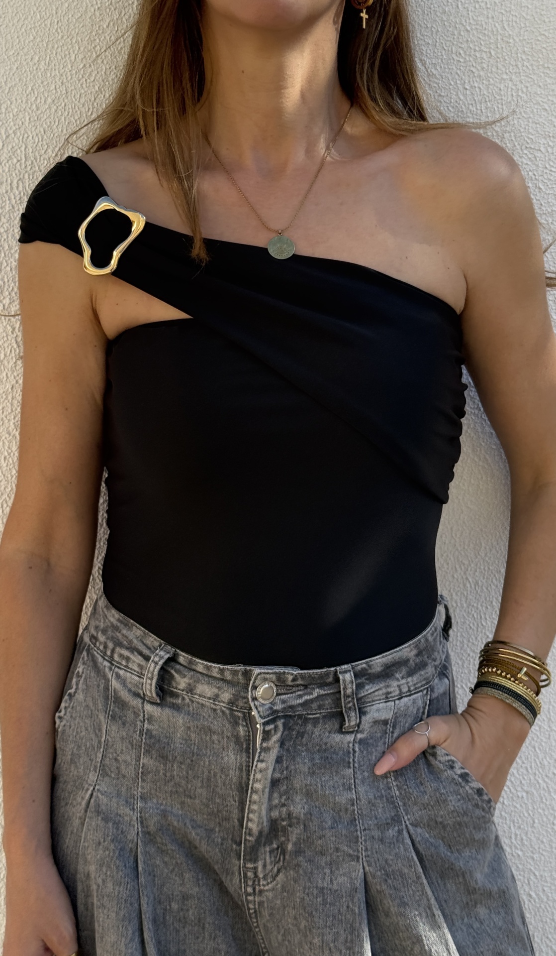 Top preto feminino de um ombro só com fivela dourada e jeans cinza claro