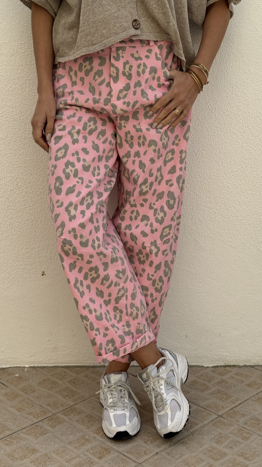 Calças rosa com padrão de leopardo cinza e bege, usadas com sapatilhas brancas em chão de azulejos
