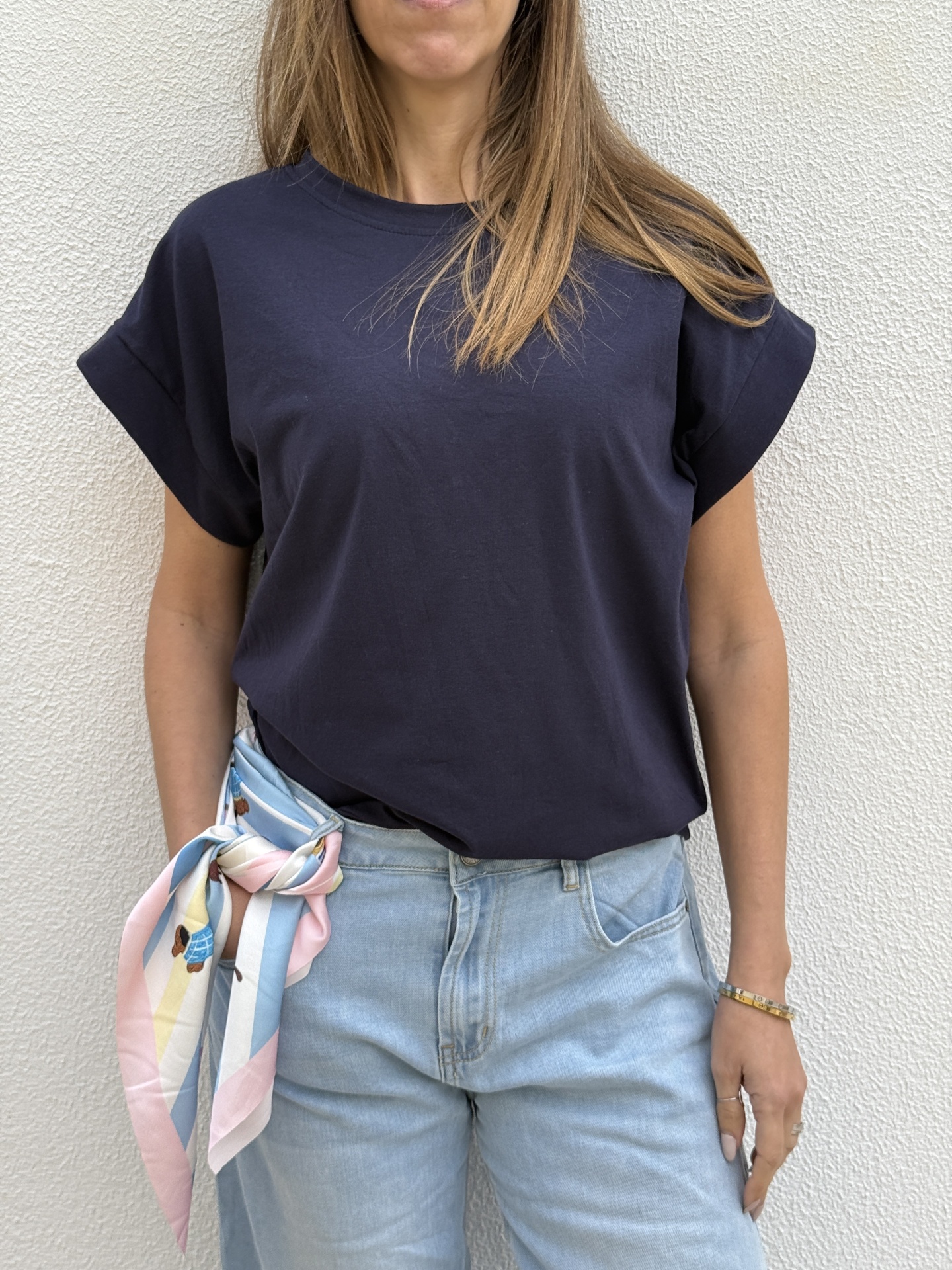 Pessoa com camisola azul escura, jeans azul claro e lenço colorido amarrado na cintura