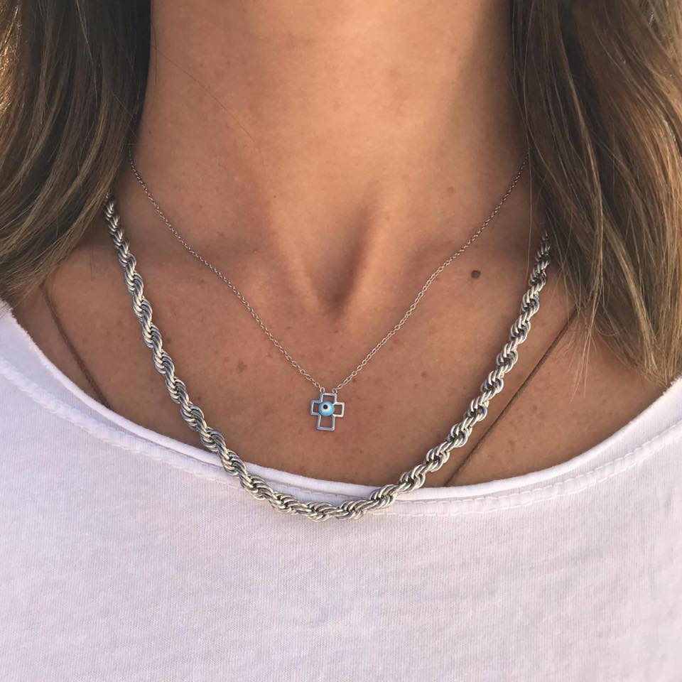 Colares prateados com pendente de cruz e corrente torcidada num pescoço feminino