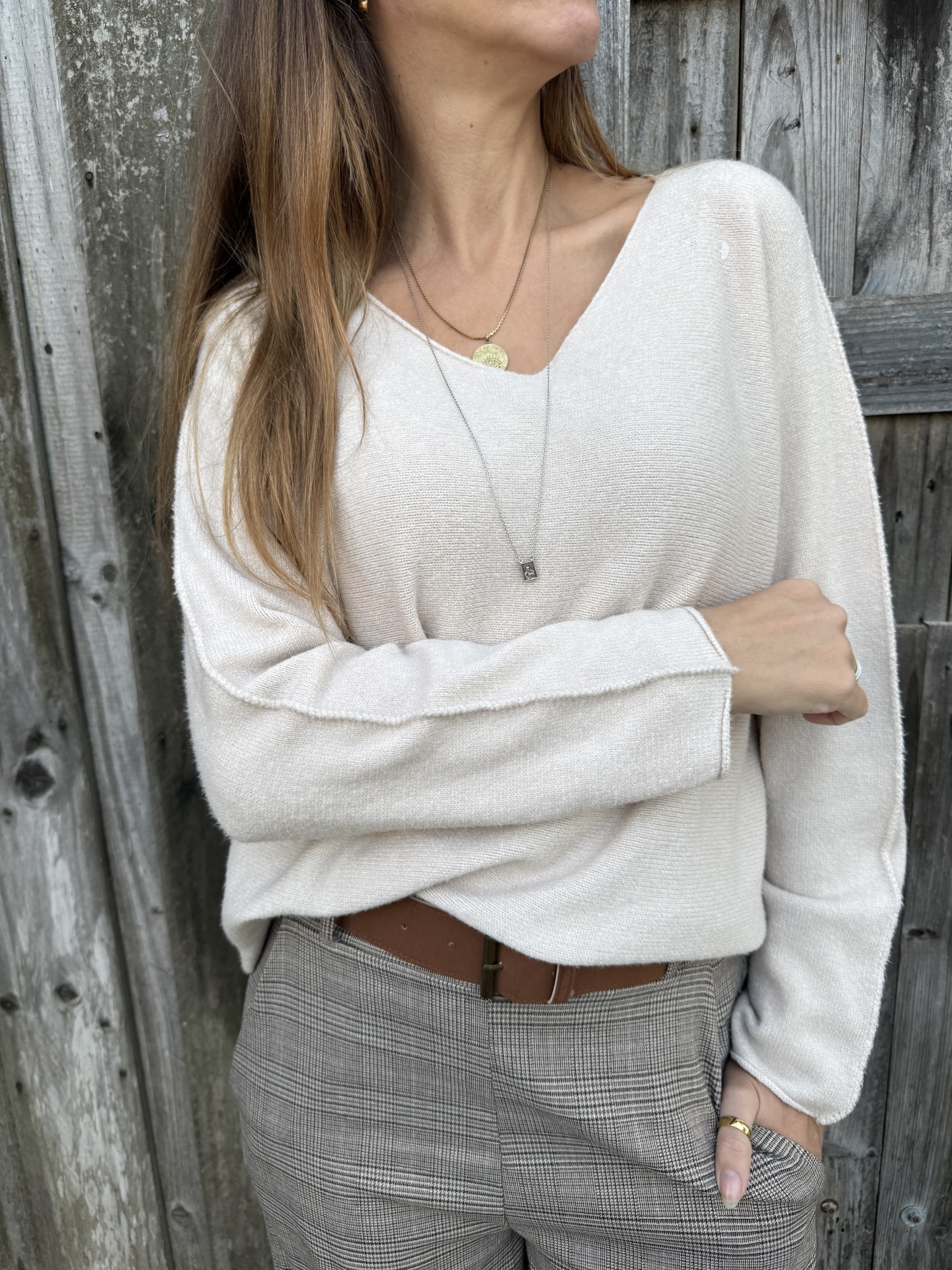 Mulher com camisola creme e calças aos quadrados cinzentas junto a parede de madeira.