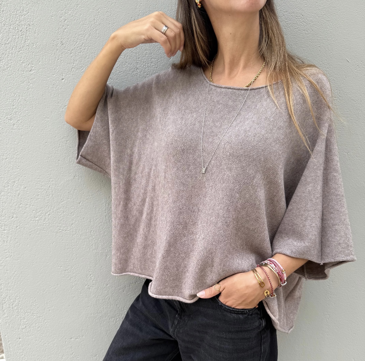 Pessoa com camisola cinza oversized e calças pretas junto a parede cinza