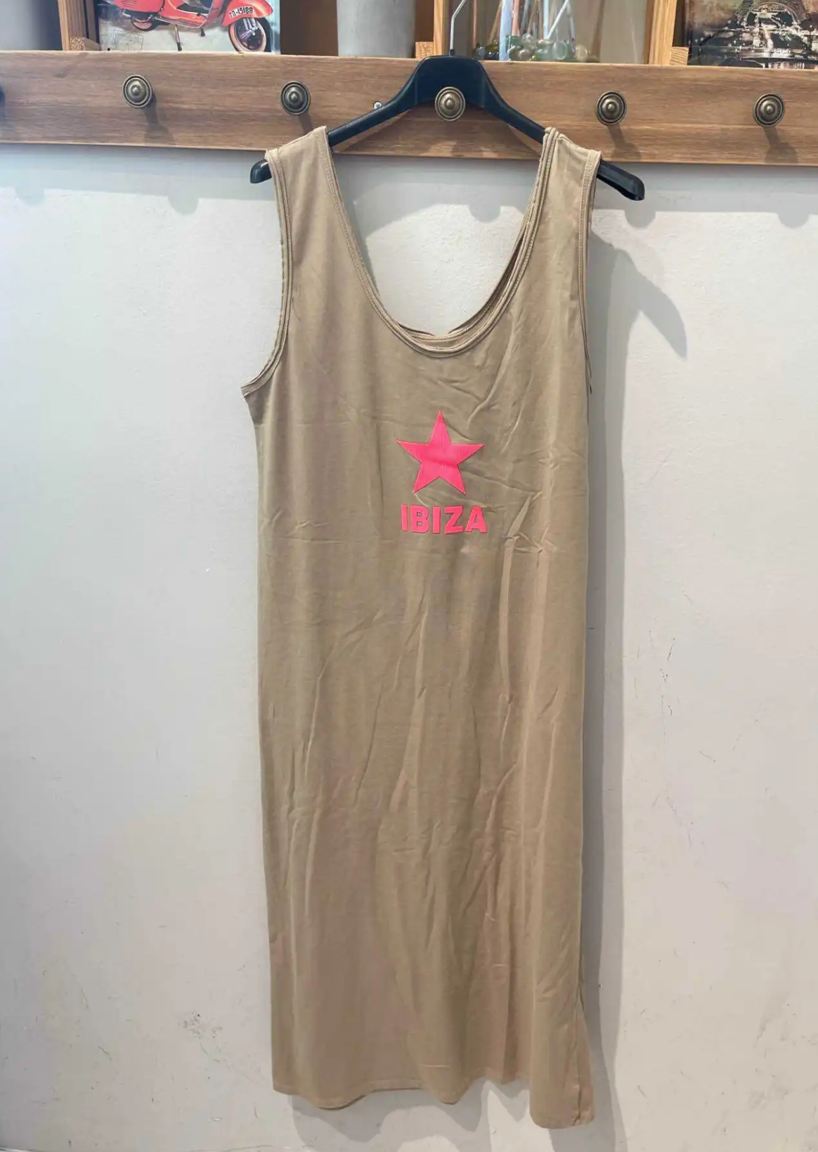 Vestido bege com estrela rosa e palavra IBIZA pendurado numa cabide preta