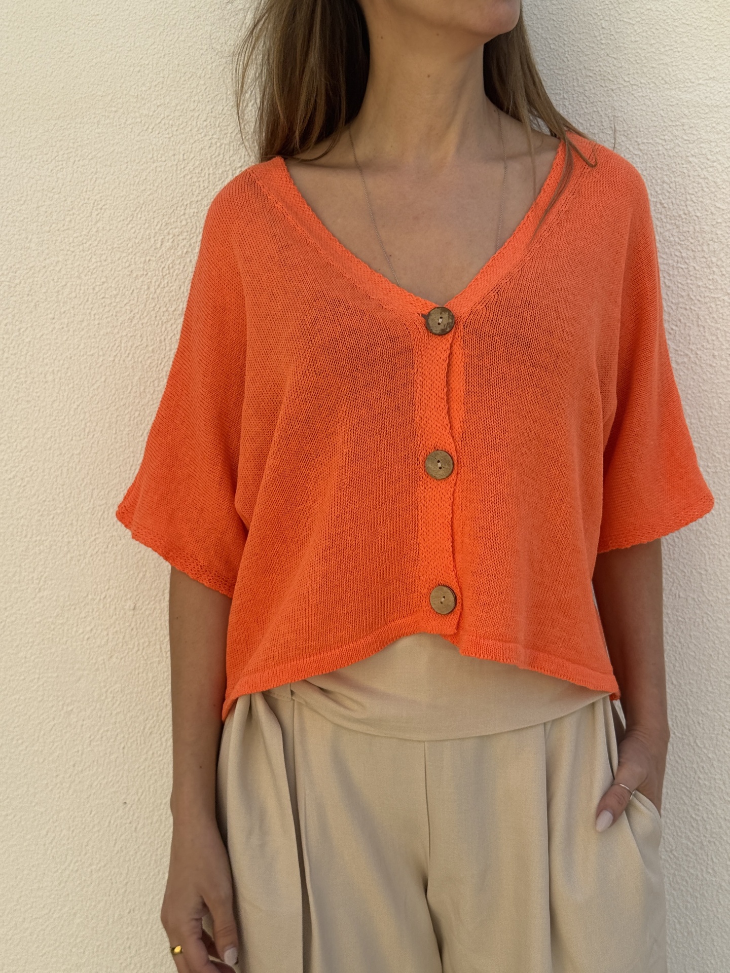 Camisola laranja de malha com botões de madeira e calças beges largas