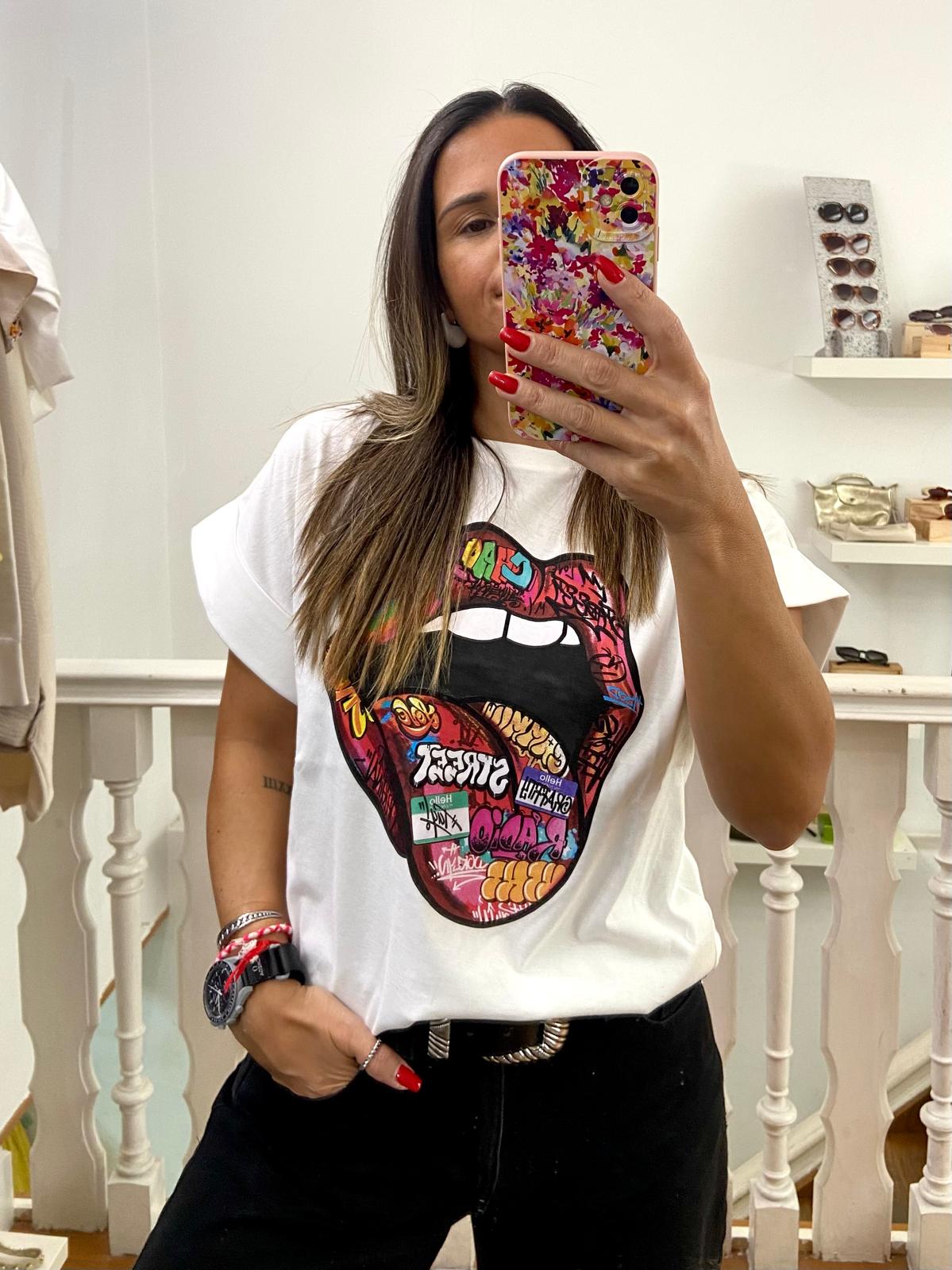 T-shirt branca com estampa colorida de boca aberta, mulher tirando selfie com telemóvel colorido em ambiente com guarda-corpo e prateleiras