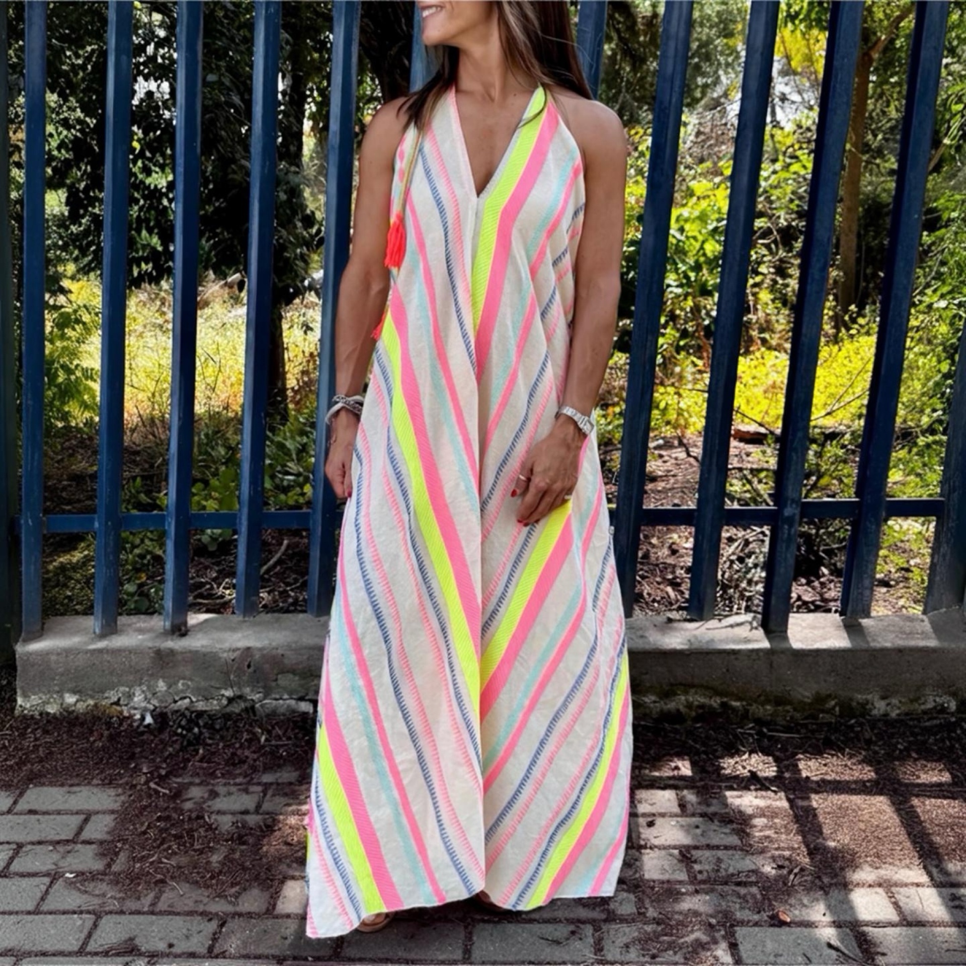 Vestido longo listrado colorido usado por mulher em zona exterior com grades azuis ao fundo