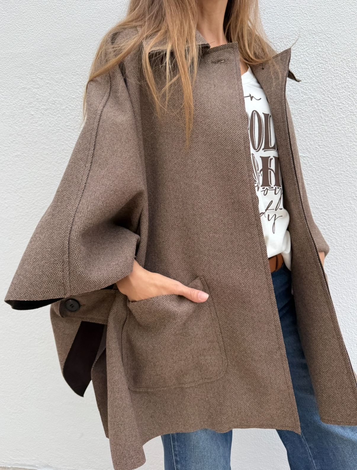 Capa castanha com padrão espinha de peixe e bolso, t-shirt branca com texto and jeans azuis.