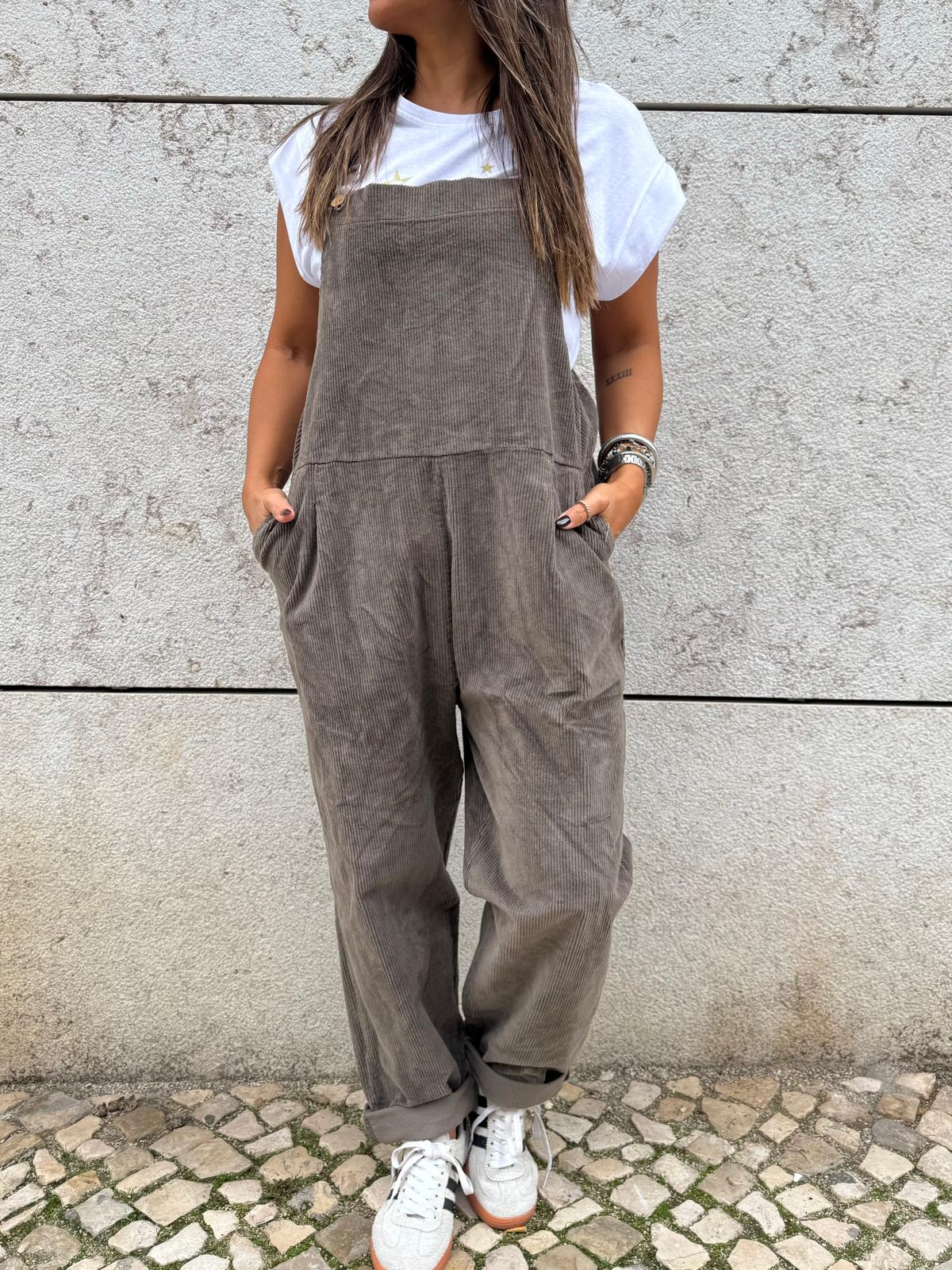 Macacão cinza com bolsos laterais e ténis brancos junto a parede de betão