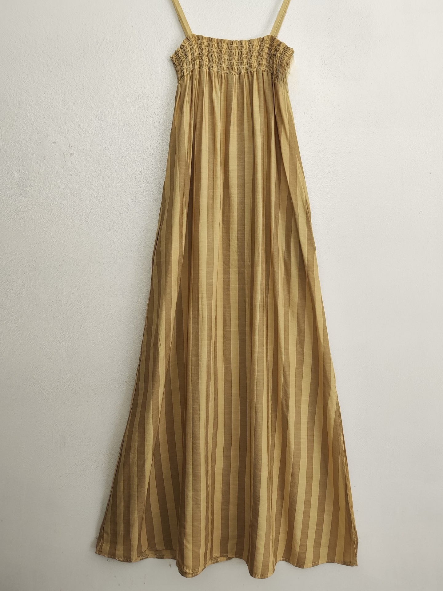 Vestido midi castanho às riscas com alças finas pendurado na parede branca