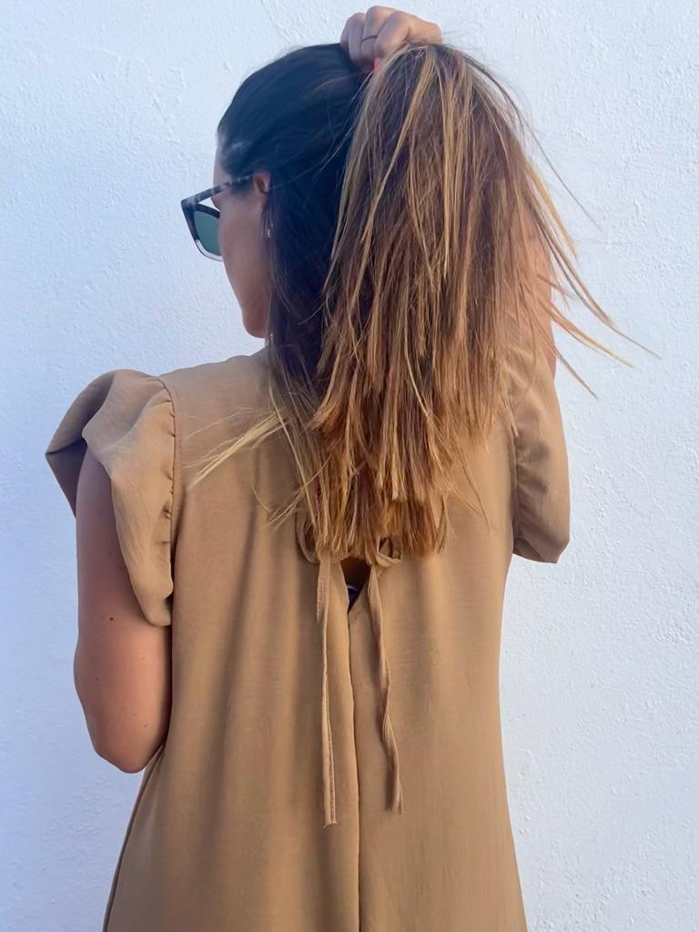 Mulher de costas a usar vestido bege com mangas franzidas e laço na parte de trás