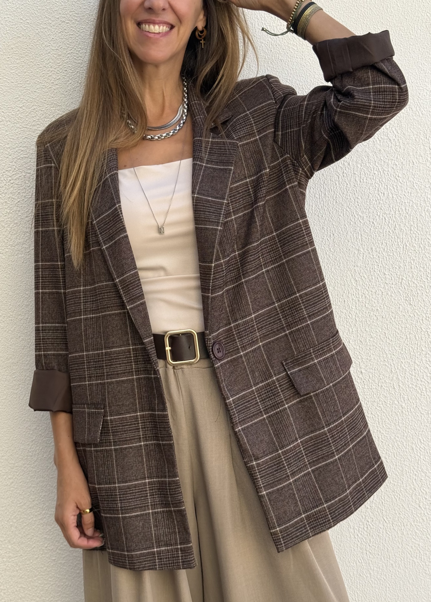 Blazer castanho xadrez com blusa branca e calças bege em fundo branco.