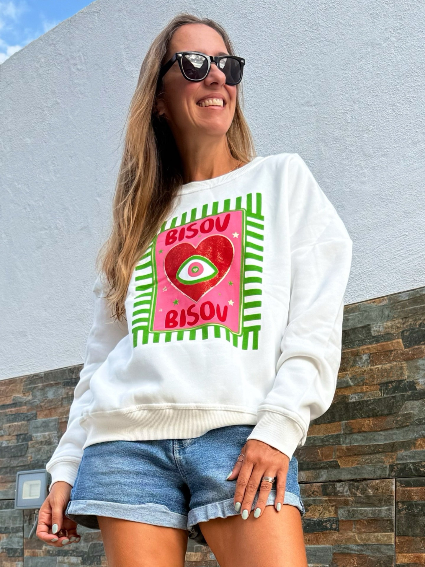 Mulher a usar sweatshirt branca com estampa colorida e calções de ganga azuis em exterior