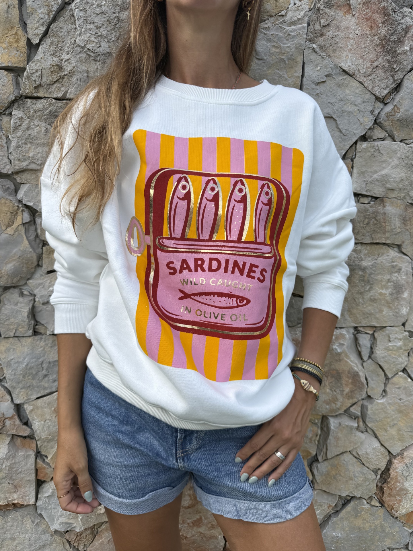 Pessoa com sweatshirt branca com estampa de lata de sardinhas em fundo listrado amarelo e rosa