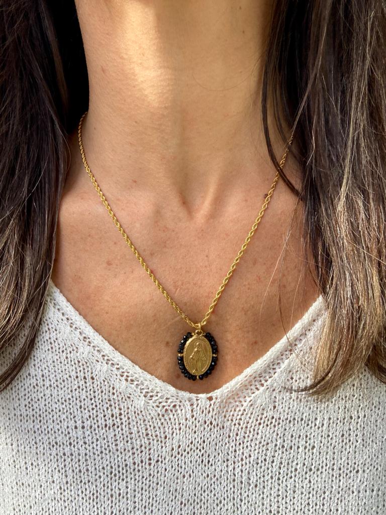 Colar dourado com pendente oval e pedras pretas numa mulher com camisola branca