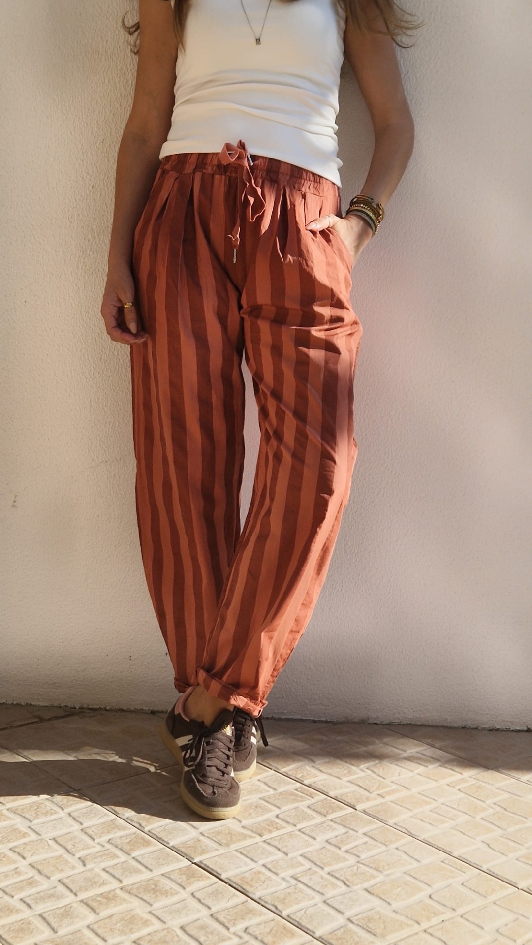 Pessoa veste calças riscas vermelhas e laranja, t-shirt branca e ténis castanhos.